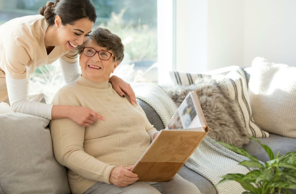 An older adult smiles, looking up at their nurse, who laughs with enjoyment as the person shares pictures with them.