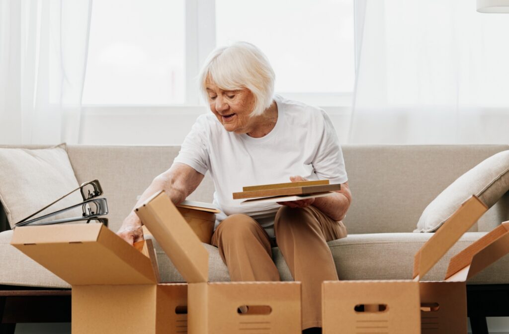 An older adult unpackes boxes while sitting on the couch in their new personal care community